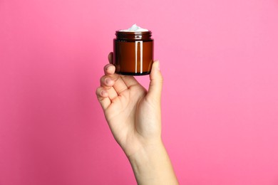 Woman holding jar of face cream on pink background, closeup