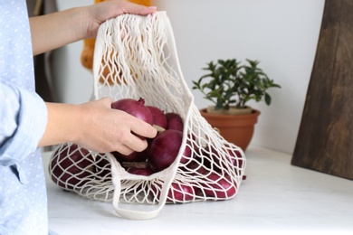 Photo of Woman taking red onion from mesh tote bag at countertop in kitchen, closeup
