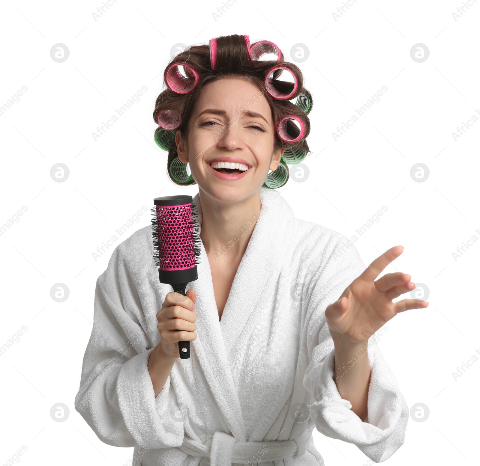 Photo of Beautiful young woman in bathrobe with hair curlers singing into hairbrush on white background