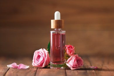 Photo of Bottle of essential rose oil and flowers on wooden table