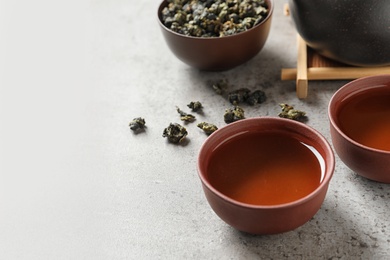 Cups of Tie Guan Yin oolong and tea leaves on grey table. Space for text