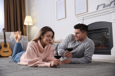Photo of Happy couple with glasses of wine resting near fireplace at home
