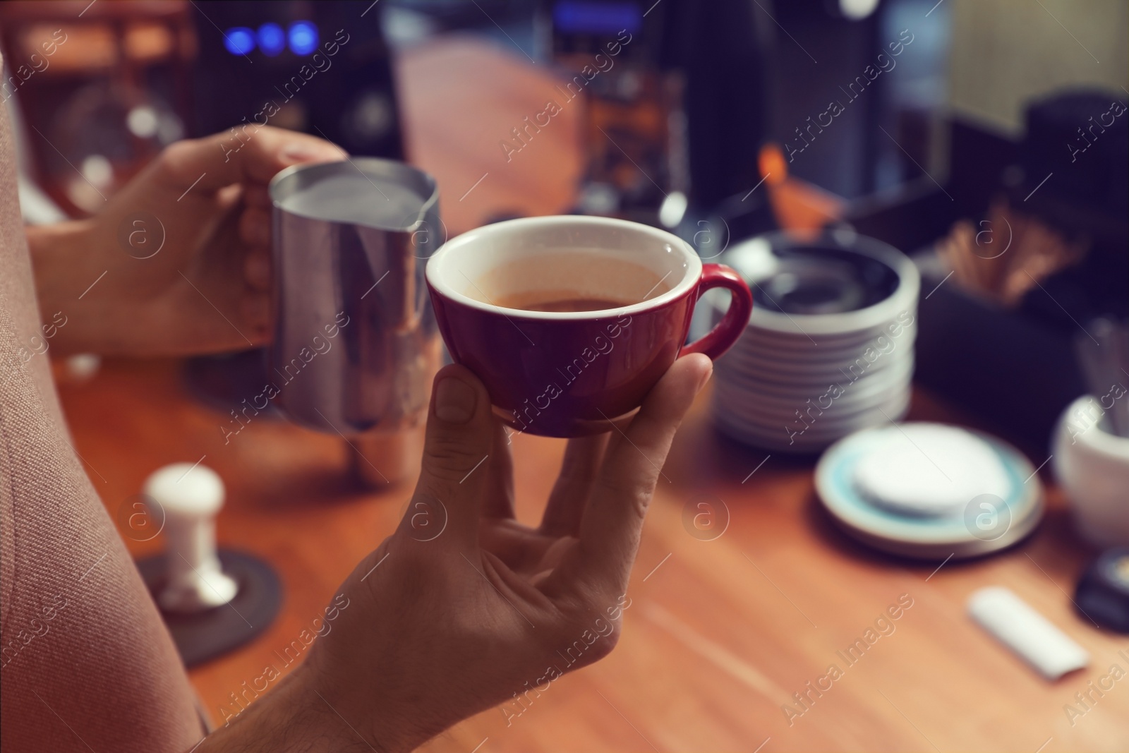 Photo of Barista holding cup of coffee and jug with milk at bar counter, closeup. Space for text