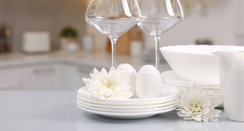 Photo of Set of clean dishware, glasses and flowers on table in kitchen. Space for text