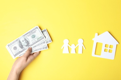 Woman with money and paper silhouettes of family and house on color background, top view. Life insurance concept