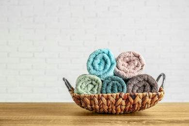 Photo of Wicker basket with rolled bath towels on wooden table near white brick wall