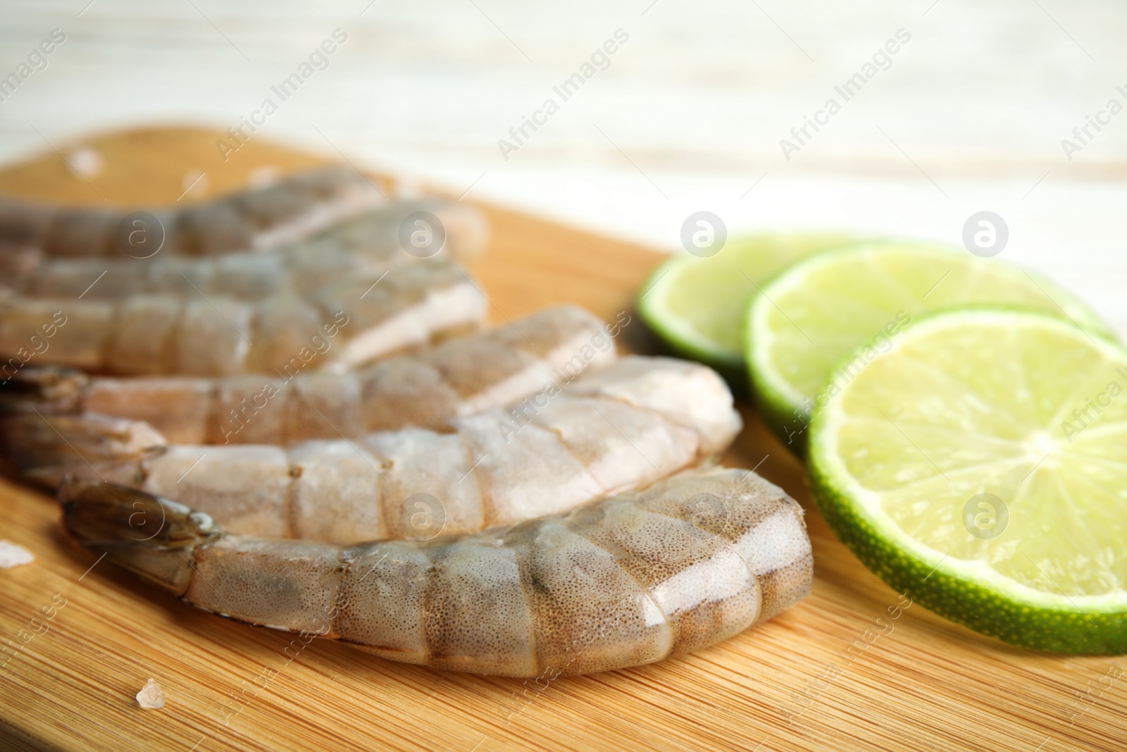 Photo of Fresh raw shrimps and lime on wooden board, closeup