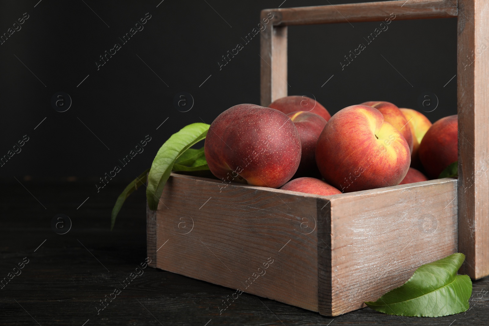 Photo of Wooden crate with tasty peaches on table against black background, space for text