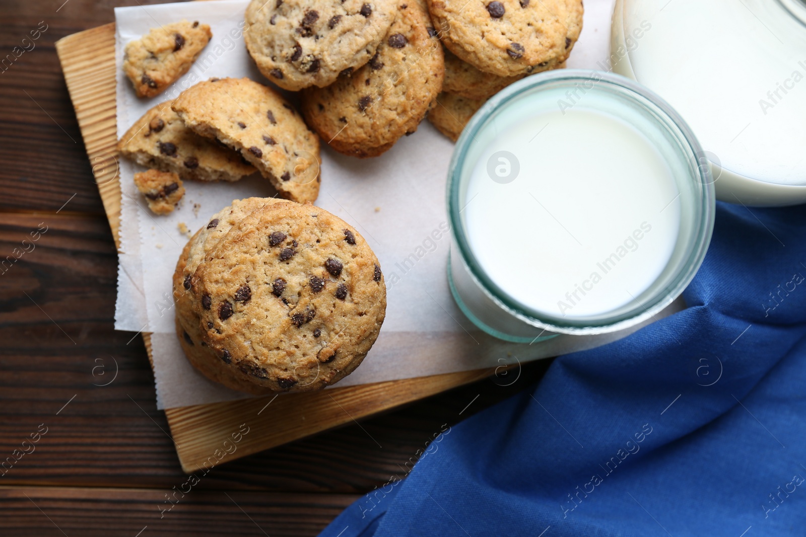 Photo of Delicious chocolate chip cookies and milk on wooden table, flat lay