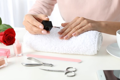 Photo of Woman applying nail polish at table, closeup. At-home manicure