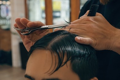 Photo of Professional hairdresser working with client in barbershop, closeup