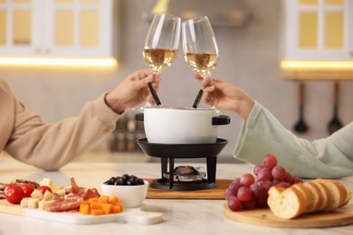 Photo of Romantic date with fondue. Couple clinking glasses of wine at home, closeup