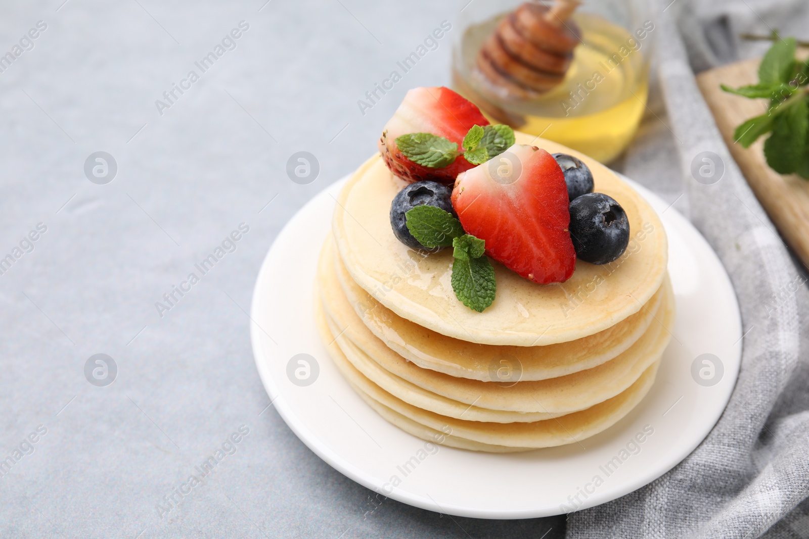 Photo of Stack of tasty pancakes with fresh berries, mint and honey on light grey table. Space for text