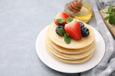 Photo of Stack of tasty pancakes with fresh berries, mint and honey on light grey table. Space for text