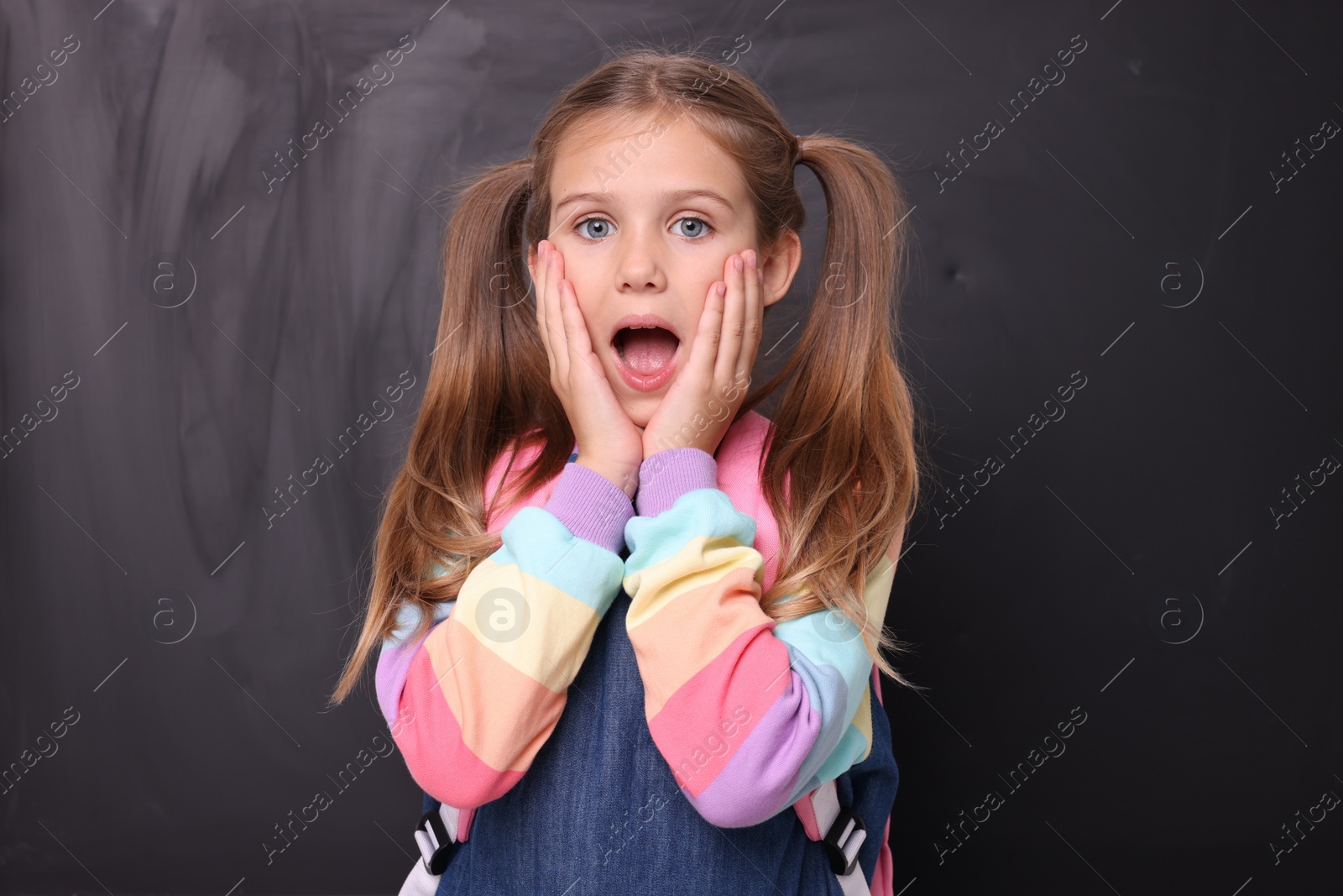 Photo of Back to school. Shocked girl with backpack near blackboard