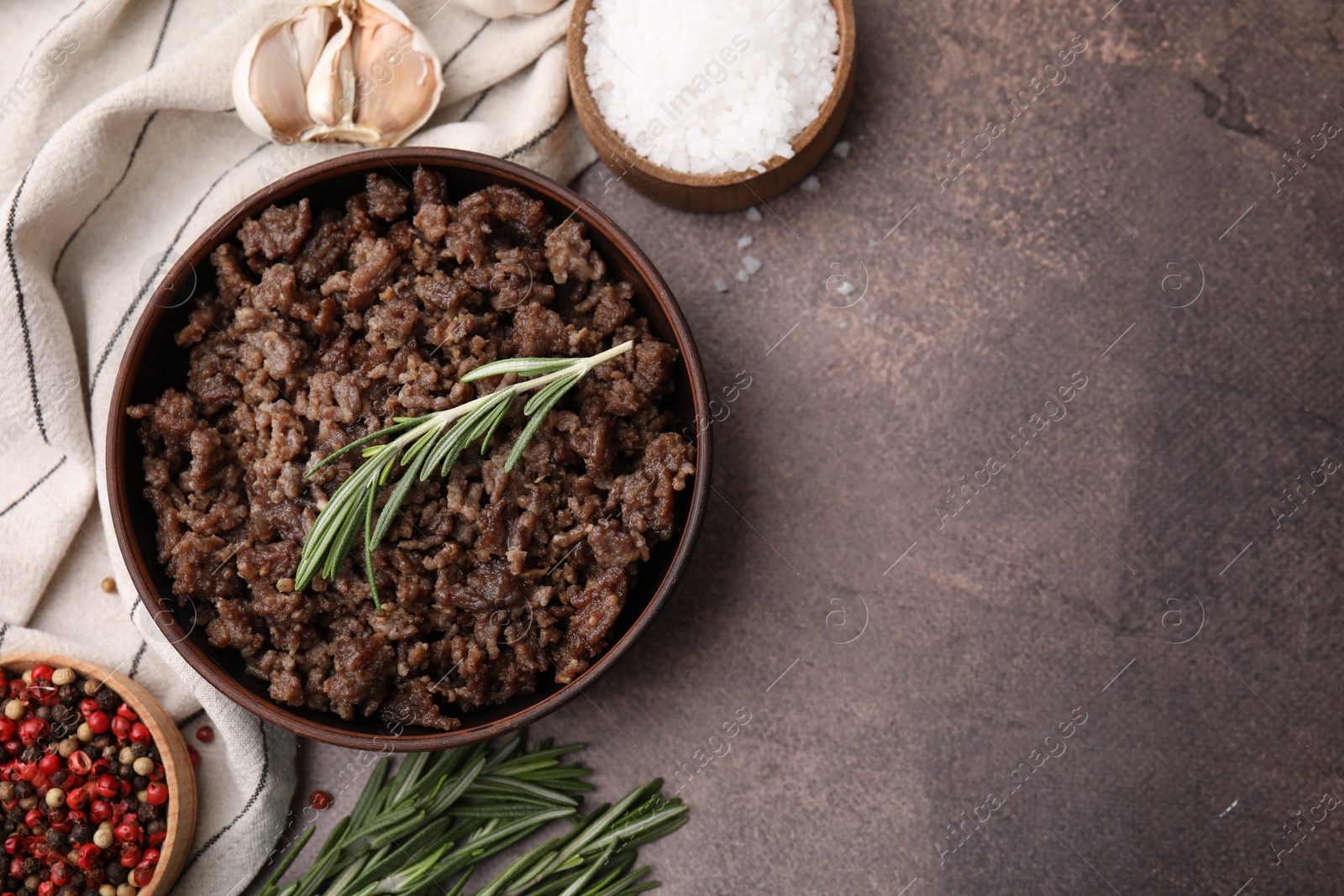 Photo of Fried ground meat in bowl and products on brown textured table, flat lay. Space for text