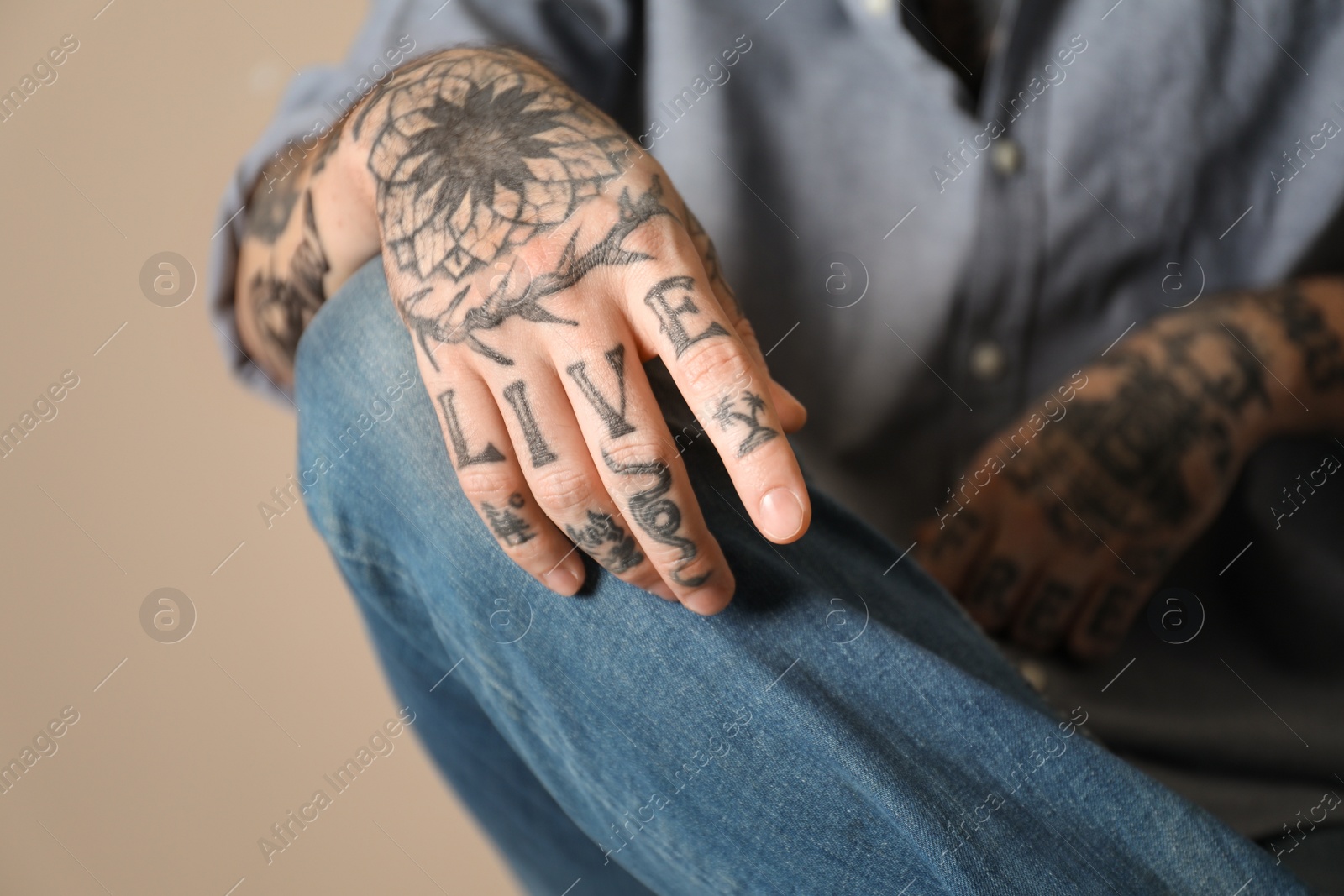 Photo of Young man with tattoos on arms against beige background, closeup