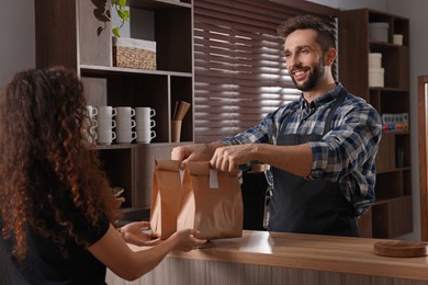 Worker giving paper bags to customer in cafe