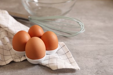 Chicken eggs, whisk, glass bowl and napkin on grey table, space for text