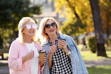 Happy mature women with coffee in park on sunny day