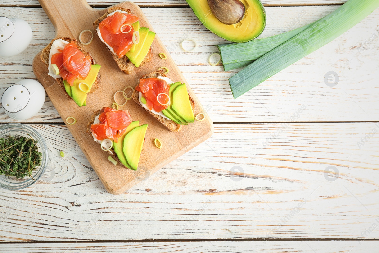 Photo of Tasty sandwiches with fresh sliced salmon fillet and avocado on wooden board, top view