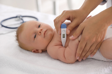 Photo of Doctor measuring temperature of little baby with digital thermometer indoors, closeup. Health care