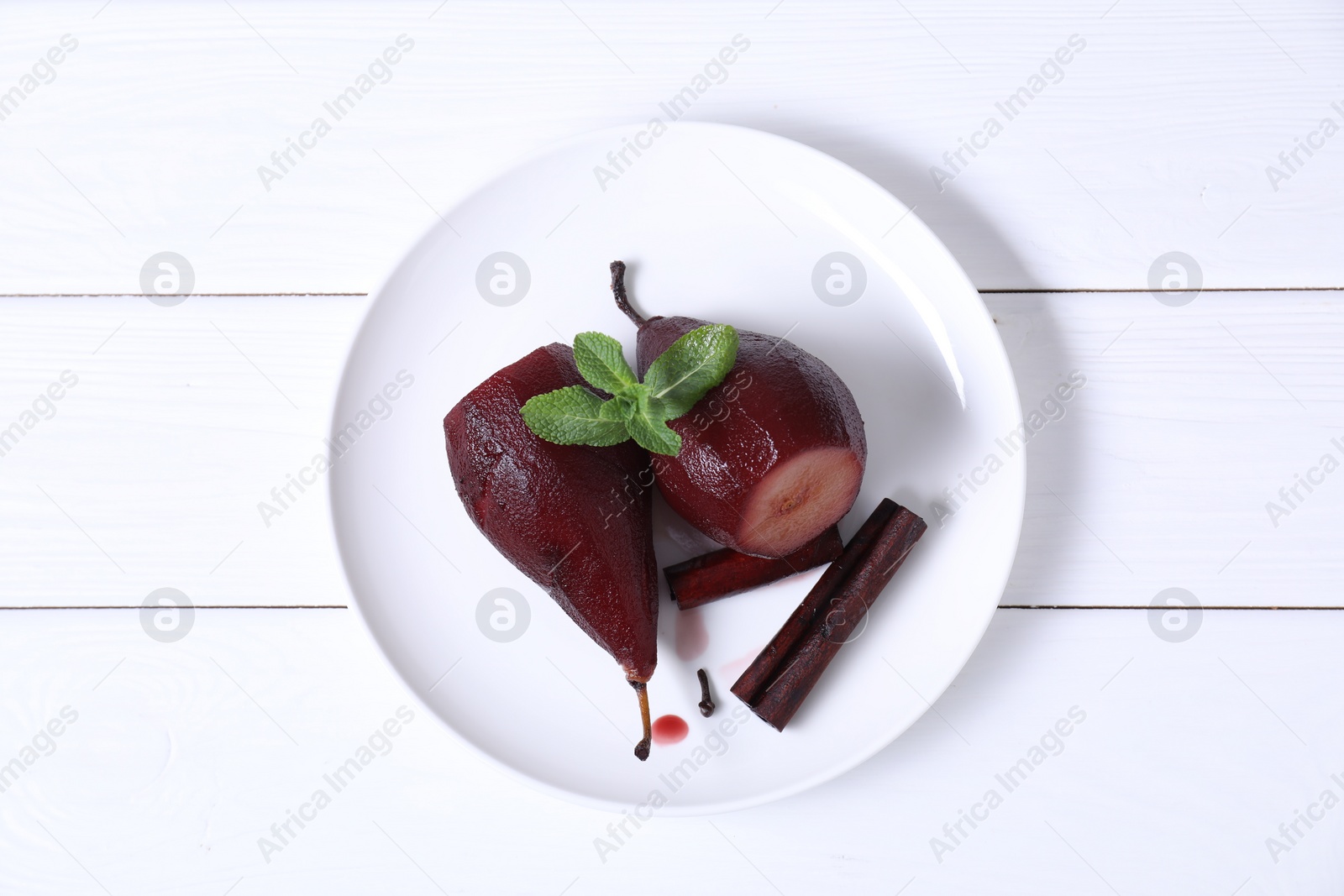 Photo of Tasty red wine poached pears with mint and cinnamon on white wooden table, top view