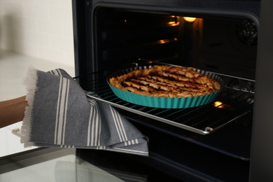 Photo of Woman taking delicious fresh homemade cake out of oven indoors, closeup