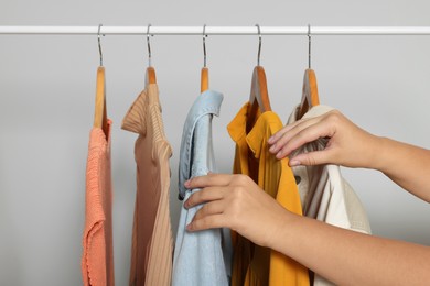 Woman taking stylish shirt from clothes rack against light grey background, closeup