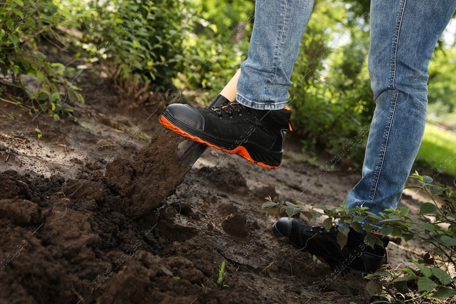 Photo of Worker digging soil with shovel outdoors, closeup