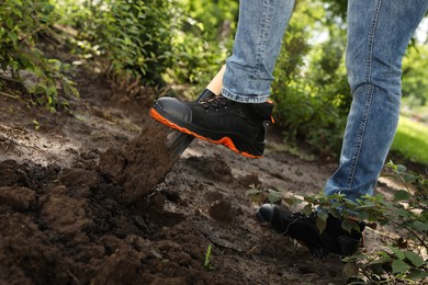 Photo of Worker digging soil with shovel outdoors, closeup