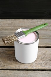 Photo of Can of pale pink paint with brush on wooden table