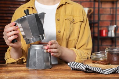 Woman making coffee in moka pot at wooden table, closeup