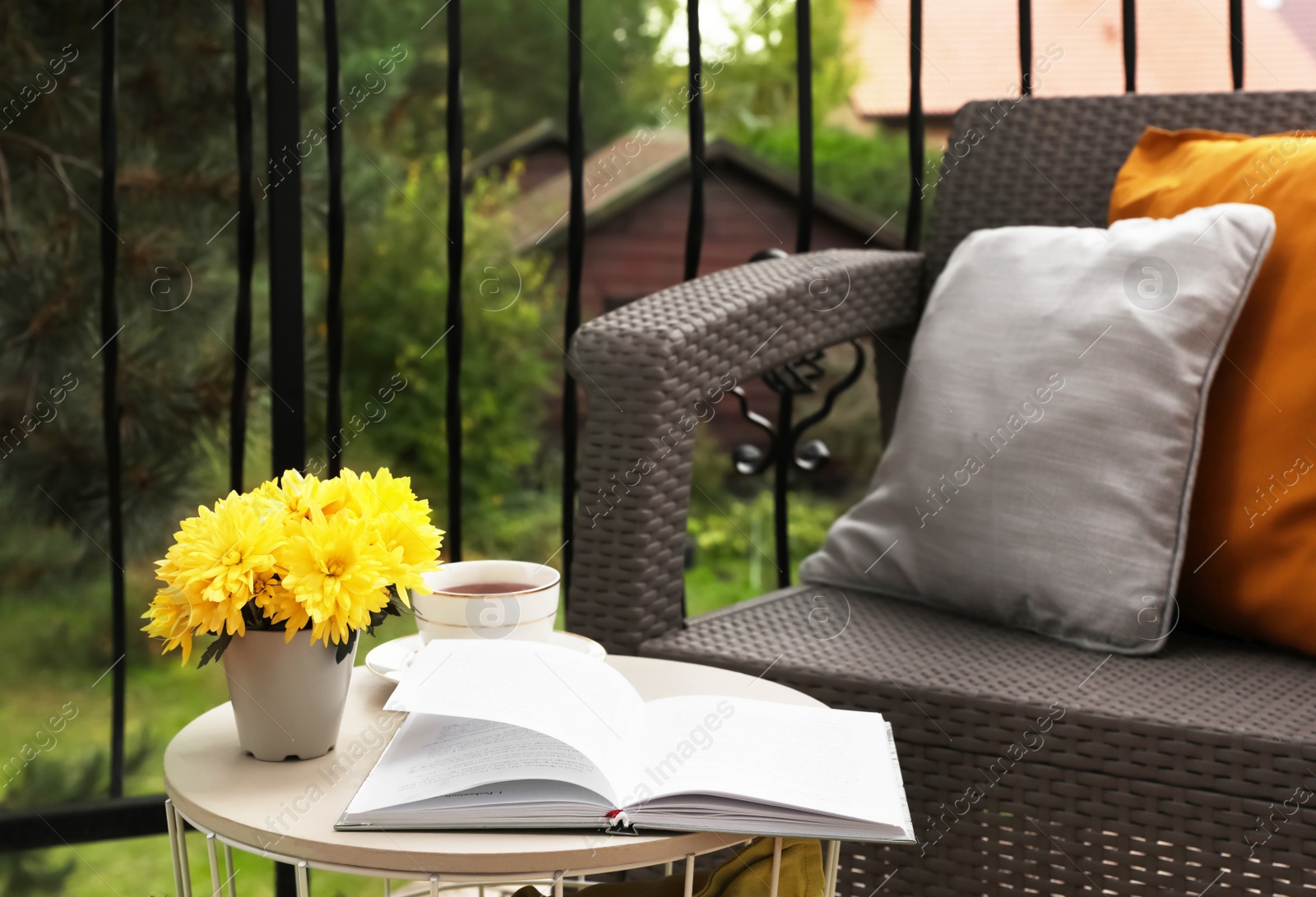 Photo of Different pillows, book and beautiful chrysanthemum flowers on garden furniture outdoors