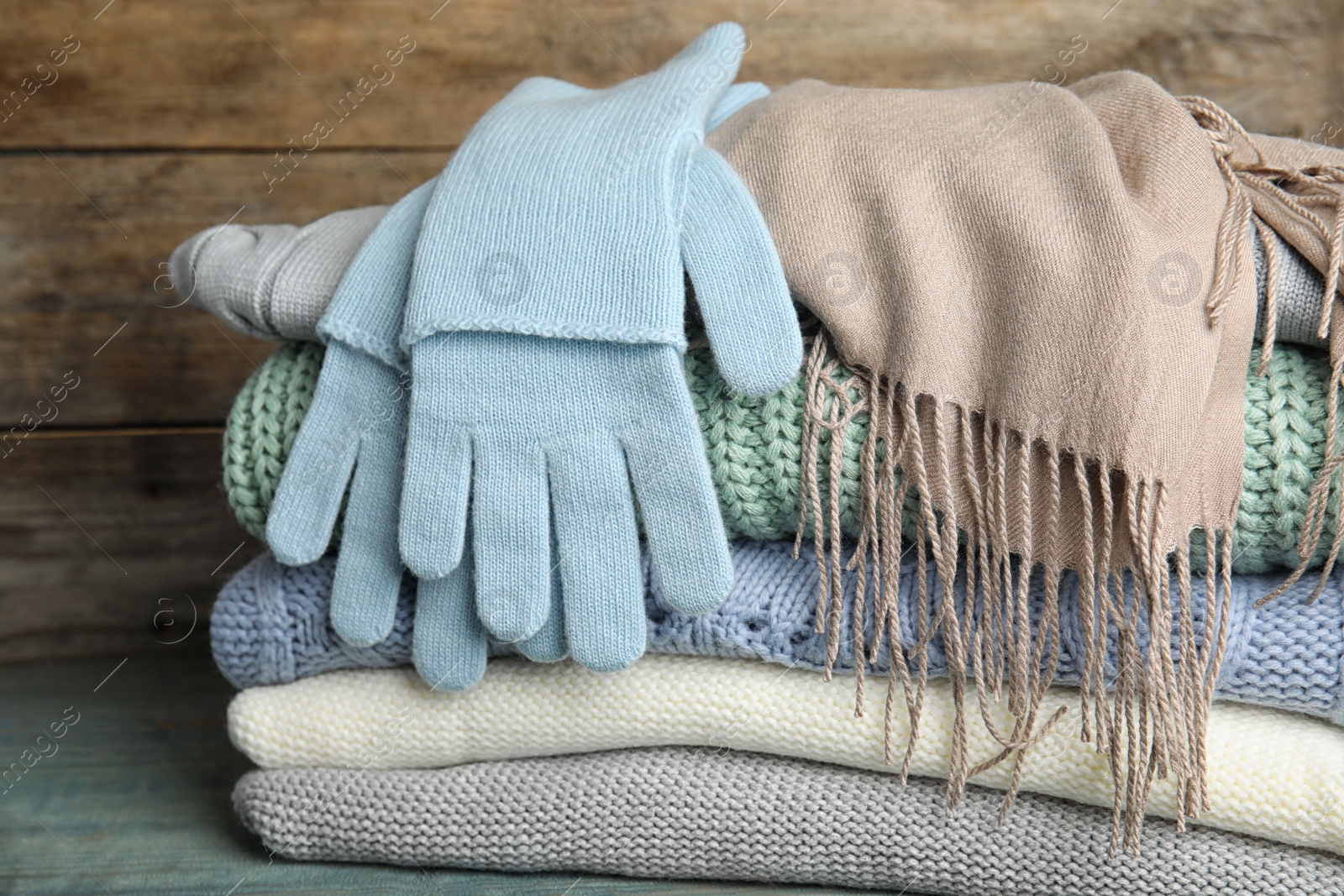 Photo of Stacked sweaters and gloves on table, closeup. Autumn clothes