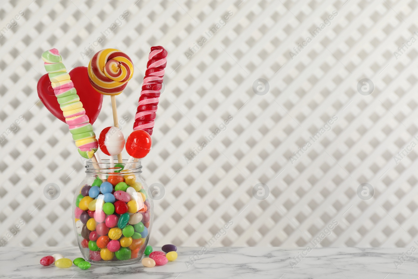 Photo of Jar with different delicious candies on white marble table, space for text