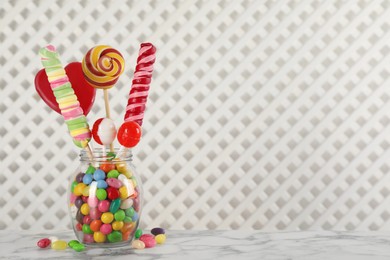 Photo of Jar with different delicious candies on white marble table, space for text