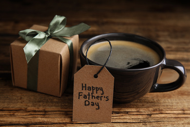 Photo of Cup of coffee, gift box and tag with phrase HAPPY FATHER'S DAY on wooden table