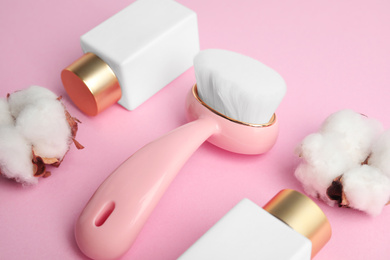 Photo of Face cleansing brush and cosmetic products on pink background