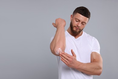 Handsome man applying body cream onto his elbow on light grey background, space for text