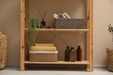 Photo of Shelving unit with soft towels in storage boxes, plant and bottles indoors