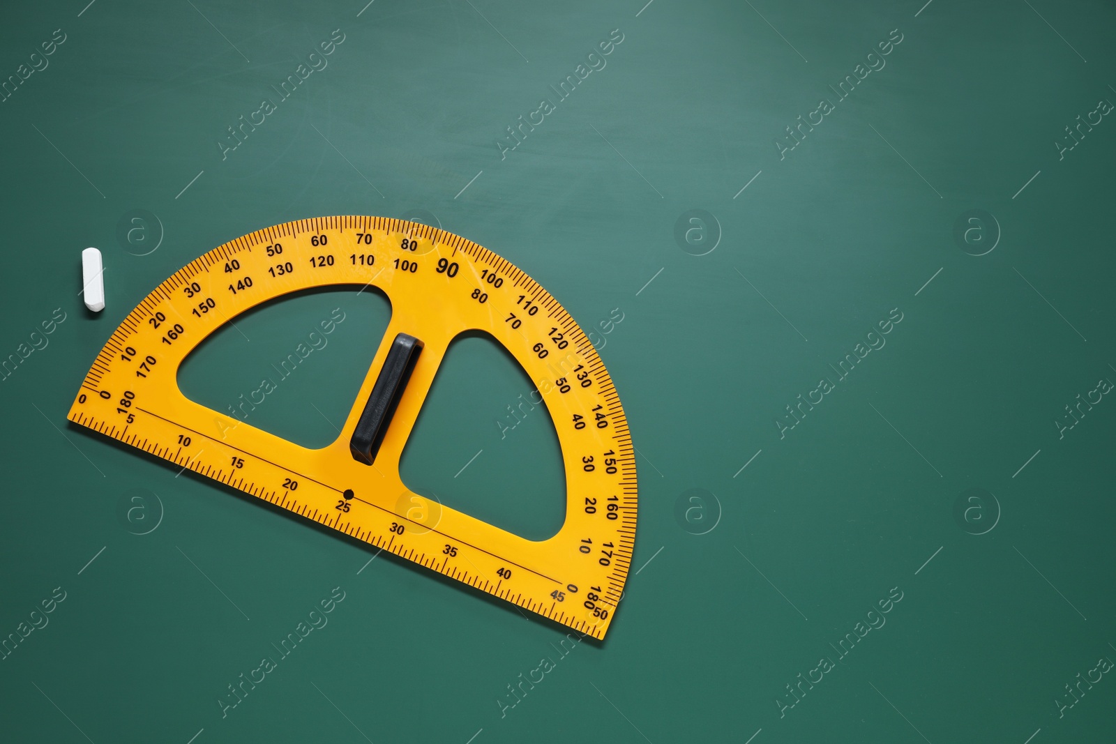 Photo of Yellow protractor and chalk on green chalkboard, flat lay. Space for text