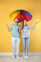 Couple with rainbow umbrella near color wall