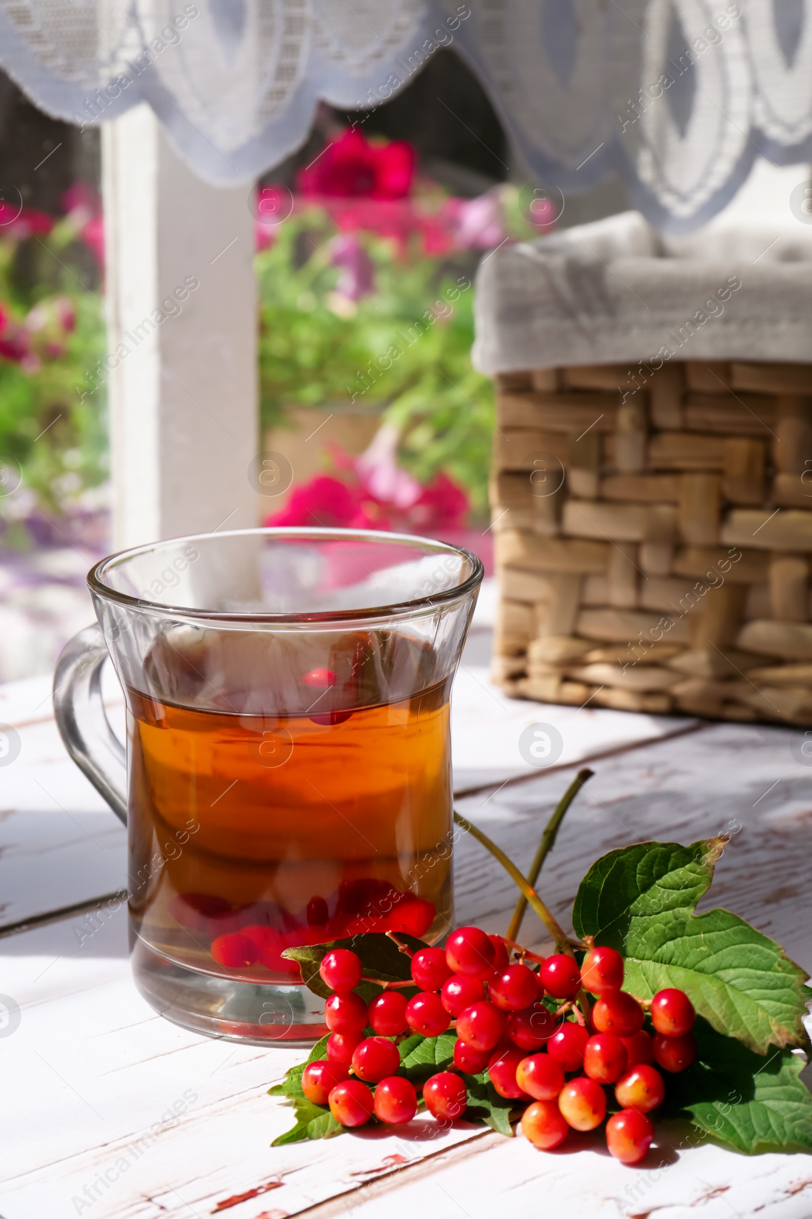 Photo of Cup of hot drink and helpful viburnum berries on white wooden table indoors