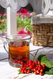 Photo of Cup of hot drink and helpful viburnum berries on white wooden table indoors