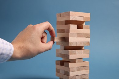 Photo of Playing Jenga. Man removing wooden block from tower on blue background, closeup