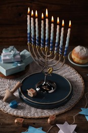 Hanukkah celebration. Menorah with burning candles, dreidels, gift boxes and donut on wooden table