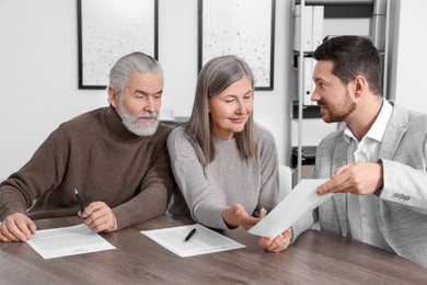 Photo of Elderly couple consulting insurance agent about pension plan at wooden table indoors