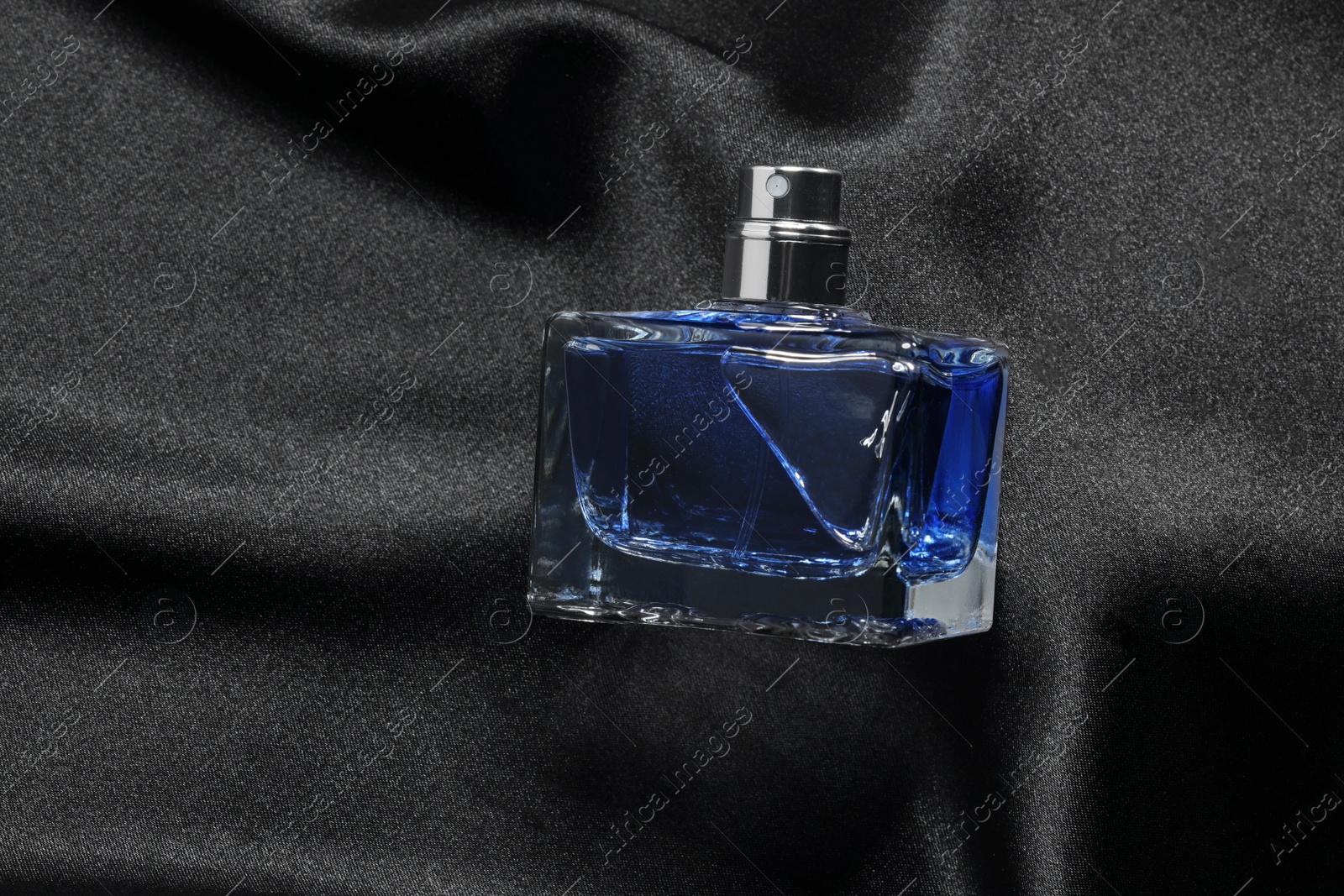 Photo of Luxury men's perfume in bottle on black satin fabric, top view