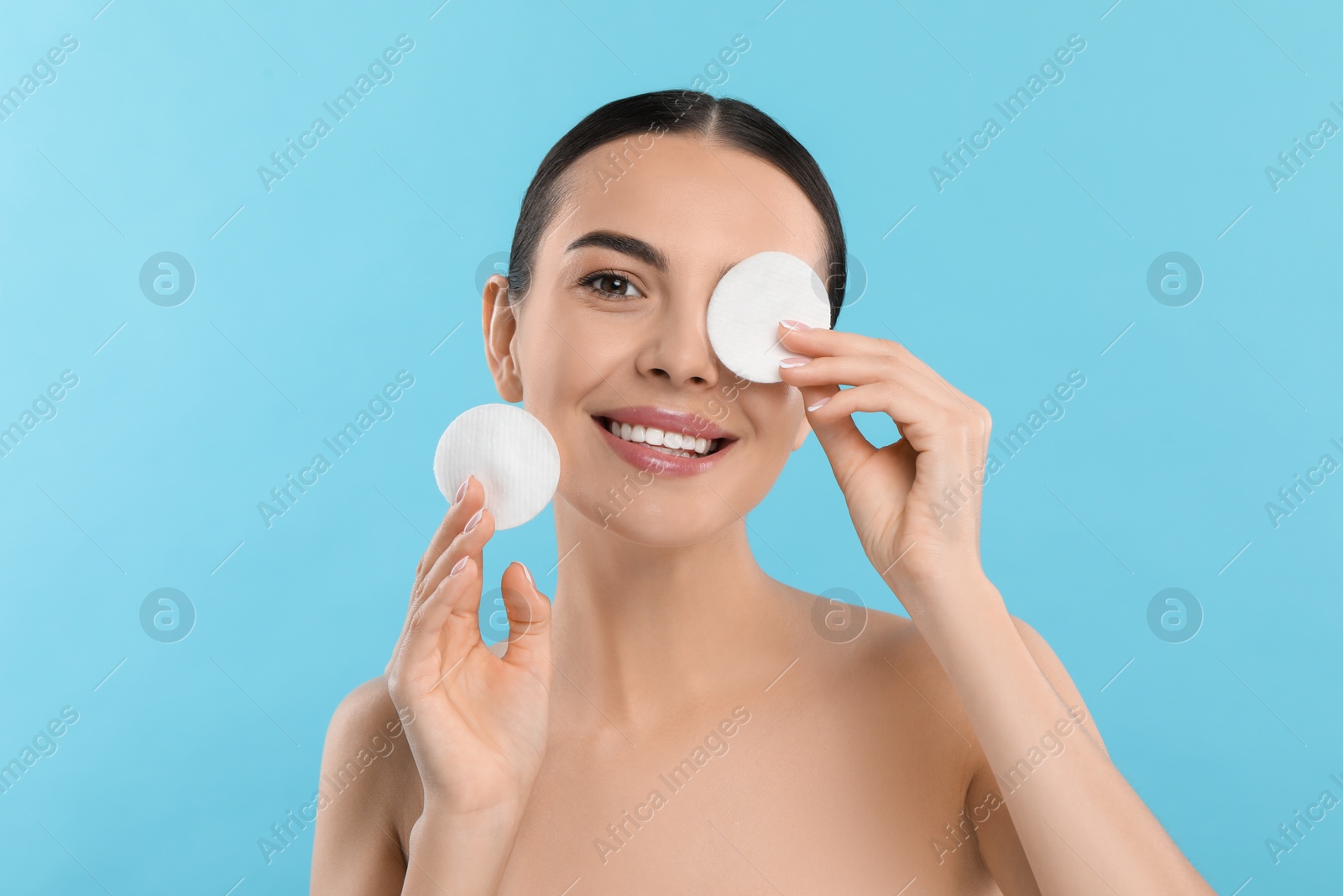 Photo of Beautiful woman holding cotton pads on light blue background. Removing makeup